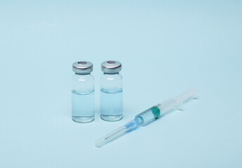 Syringe with two vials of vaccine liquid on a blue background