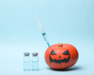 Halloween pumpkin with syringe and vaccine bottles on blue background