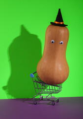 Obraz premium Mini shopping cart with halloween pumpkin on green purple background. Creative halloween layout