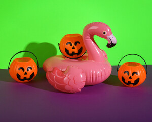 Halloween creative still life with inflatable flamingos and halloween pumpkins candy buckets on green purple background
