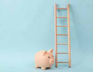 Wooden ladder and piggy bank on blue background. Minimum layout. Business, leadership concept,...
