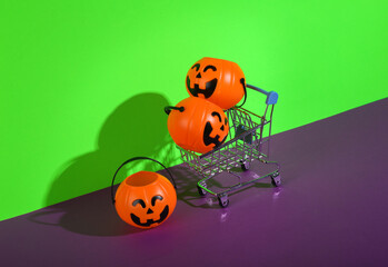Shopping cart with halloween buckets on green purple background. Creative halloween layout, sale, shopping concept