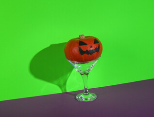 Halloween party. Halloween pumpkin with cocktail martini glass on green purple background. Minimal layout