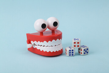 Funny toy clockwork jumping teeth with eyes and dice on blue background.