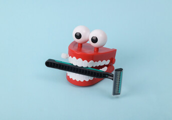 Funny toy clockwork jumping teeth with eyes holding razor on blue background.