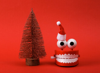 Funny toy clockwork jumping teeth with eyes, santa hat and christmas tree on red background.