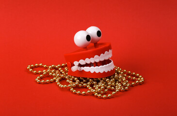 Funny toy clockwork jumping teeth with eyes and christmas garland on red background.