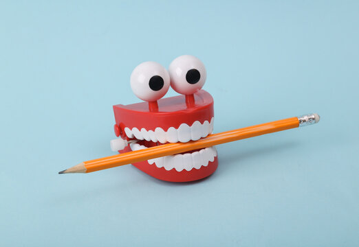 Funny toy clockwork jumping teeth with eyes holding pencil on blue background.
