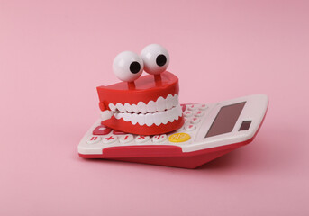 Funny toy clockwork jumping teeth with eyes on calculator, pink background.