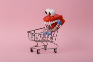Mini shopping cart with clockwork jumping monster teeth on pink background