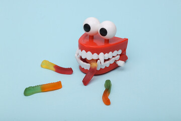 Funny toy clockwork jumping monster teeth with eyes eats gummy worms on blue background