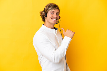 Telemarketer man working with a headset isolated on yellow background proud and self-satisfied