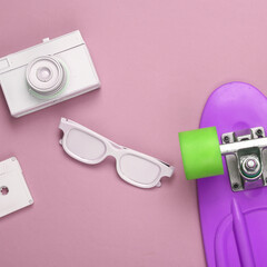 Minimalistic layout of white audio cassette, glasses, camera and penny board on purple background. Top view. Flat lay