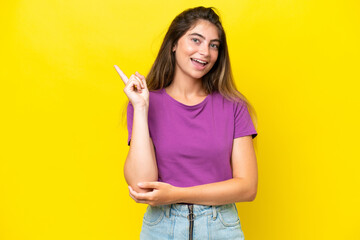 Young caucasian woman isolated on yellow background happy and pointing up