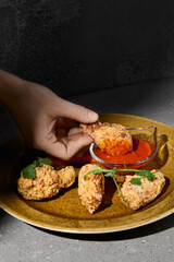 American appetizers buffalo wings with vegetables and sauce on gray stone table. Bbq wings in woman hand on concrete background with hard shadow. Female hand holding chicken wings. Junk food.