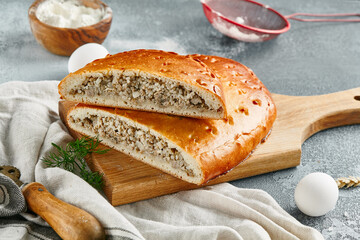 Classic pie with minced meat and rice on wooden board. Composition with meat pie on concrete background with textile and spices. Homemade pie with meat and rice in rustic style on gray table.