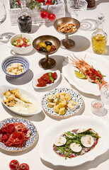 Italian food - antipasti on white table on sunny day. Assorted appetizers in italian style with shadows. Aesthetic composition with antipasti and delicatessen. Wedding food. Trattoria menu.