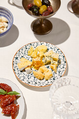 Cheese platter on white table with hard shadow. Cheeseboard with parmesan, gorgonzola, brie. Cheese appetizer in Italian menu. Aesthetic food composition with cheese assorted. Sunny day in tuscany.