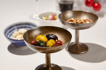 Italian antipasti from olives mix and spices. Marinated olives in metal bowl on white table with shadows. Aesthetic composition with green and black olives. Lunch in Tuscany.