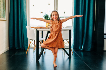 Funny adorable happy kid girl jump at home indoors, cute little child having fun dancing to music playing indoors alone enjoy pretending dancer in the morning