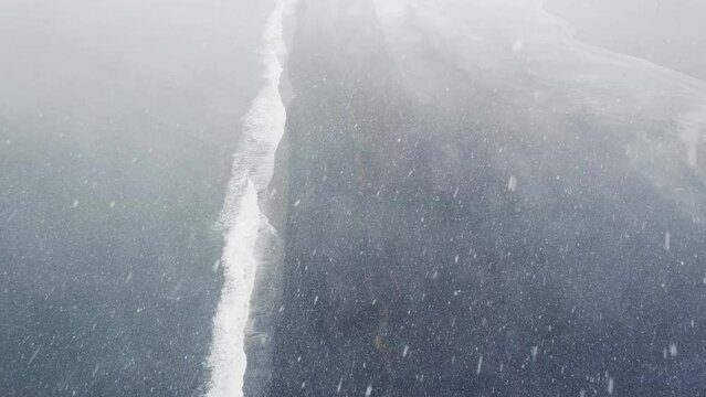 Snow storm over Hvalnes black sand beach in Iceland, High angle drone aerial view