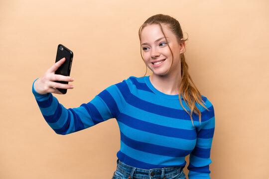 Young caucasian woman isolated on beige background making a selfie
