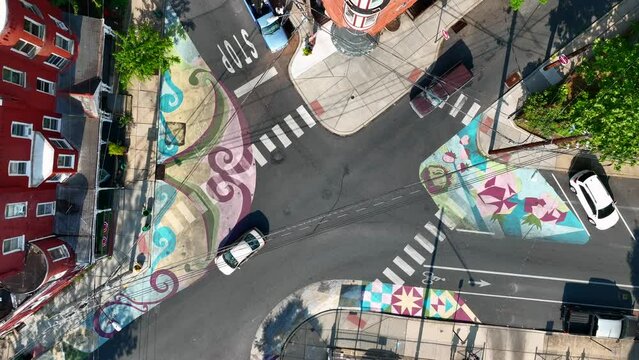 Colorful crosswalks with street mural in urban city. Cars drive along quiet streets lined with brick apartments and townhomes. Top down aerial shot.