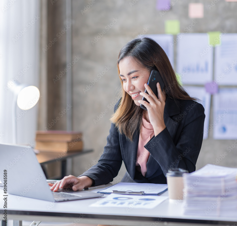 Wall mural young business asian woman talking on smartphone and working in office. asian female business sittin