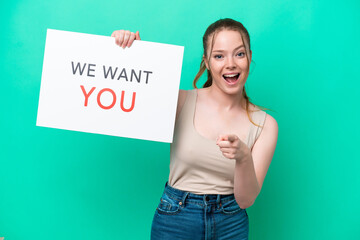 Young caucasian woman isolated on green background holding We Want You board and pointing to the...