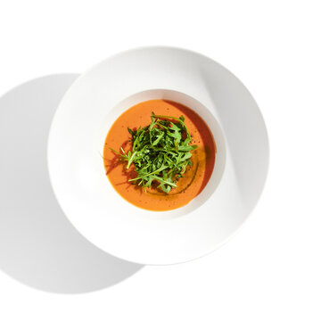 Summer Spanish soup - gazpacho with rocket salad isolated on white background. Vegetarian cold tomato soup in white plate. Meatless food in menu. Veggie lunch. Healthy food. Plant based eating.