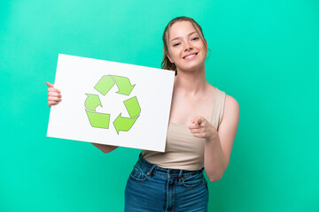 Young caucasian woman isolated on green background holding a placard with recycle icon and pointing to the front