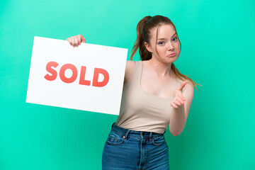 Young caucasian woman isolated on green background holding a placard with text SOLD making a deal