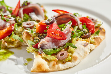 Tapas with avocado cream, anchovy, paprika and kalamata olives on focaccia. Bruschetta with guacamole and anchovy isolated on white background. Appetizer contemporary concept. Fish antipasti.