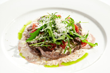 Meat medallions with mushroom creamy sauce and rucola salad on white background. Meat steak on mushroom gravy with tomato and rocket salad. Roasted beef fillet with salad in restaurant menu.