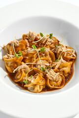 Main course in italian cuisine - meat tortellini with demi-glace sauce and mushroom cream. Beef ravioli on white plate. Tortellini with minced veal in beef sauce. Gourmet cuisine in restaurant menu.