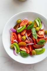 Top view of fresh summer tomatoes vegan salad with basil olives red onions in white bowl food