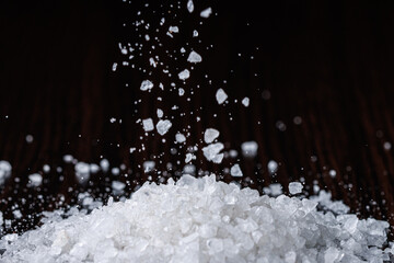 Coarse-grained sea salt is poured into a pile against the background of a black table. Selective...