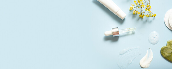 Serum in dropper and moisturizing smears cosmetic cream with facial massager on colored background. Top view