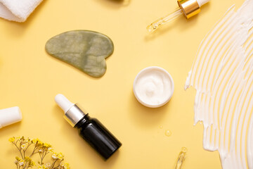 Serum and moisturizing cosmetic cream with facial massager on colored background. Top view