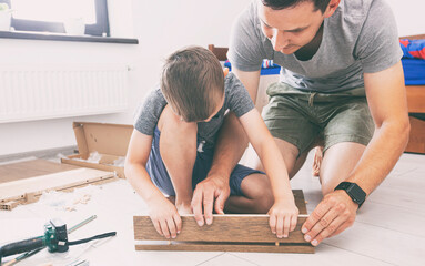 Father and son assembling the desk together and father teaches his son how to use tools