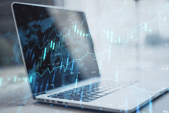 Close up of laptop on desktop with creative glowing forex chart hologram and map on blurry background. Stock, market and invest concept. Double exposure.