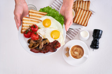 Fried eggs, bacon, tomato, toasted bread in white ceramic plate and cup of coffee