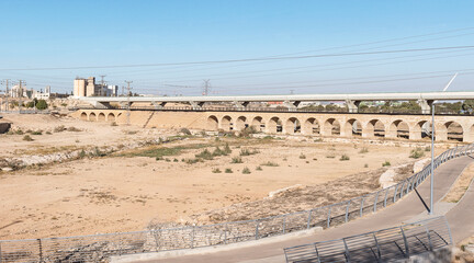 a modern train bridge spans the Beer Sheva River in front of the ancient Ottoman era train bridge with a modern bike path in the foreground