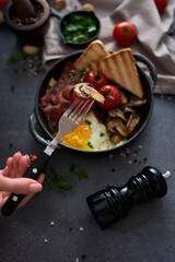 Fried eggs, bacon, tomato and toasted bread in a black ceramic pan at domestic kitchen