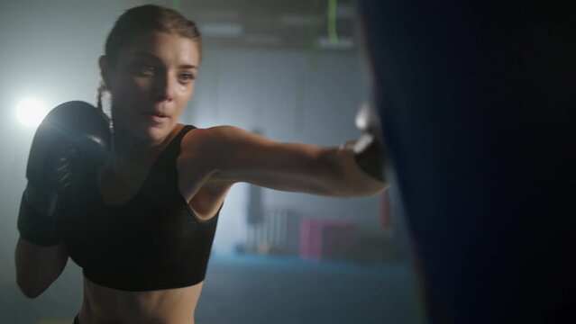 Woman power, female fighter beats a punching bag, trains his punches, training day in the boxing gym, the female strikes fast, cinematic lighting.