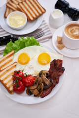 Fried eggs, bacon, tomato, toasted bread in white ceramic plate and cup of coffee