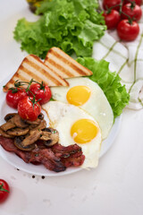 Fried eggs, bacon, tomato and toasted bread in white ceramic plate
