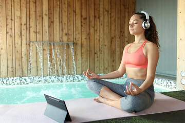 Woman e-learning yoga using laptop and headphones to meditate