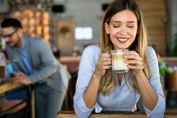 Portrait of happy young business woman drinking coffee in a break. In the background, her colleagues