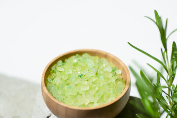 Wooden bowl with green bath sea salt with rosemary branch. Beauty treatment for spa and wellness on grey and white background. Skincare natural cosmetic concept for body care